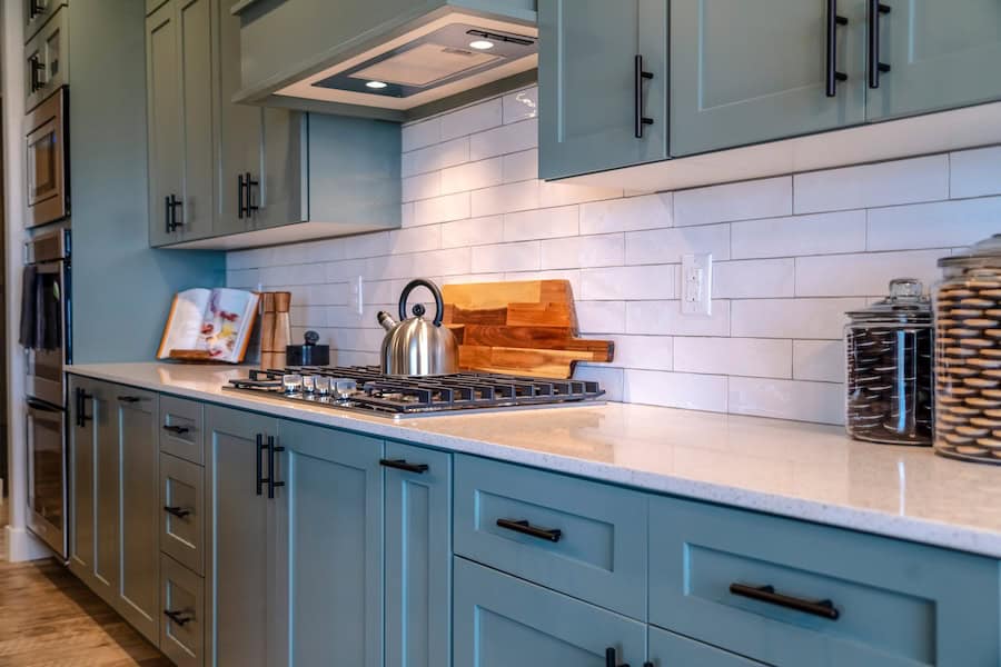 A kitchen cooking area with blue, wood-based cabinets.