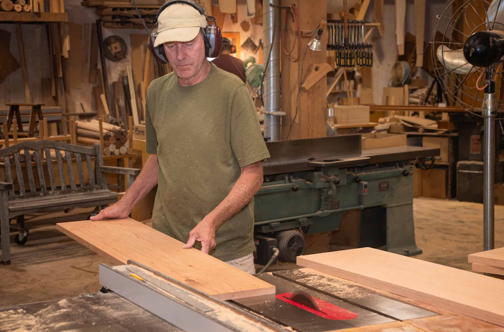 Furniture maker feeding a board through a tablesaw in woodshop.