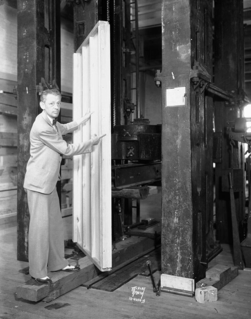 Forest Products Laboratory engineer George W. Trayer pointing to a newly developed plywood panel in a large testing machine, 1933