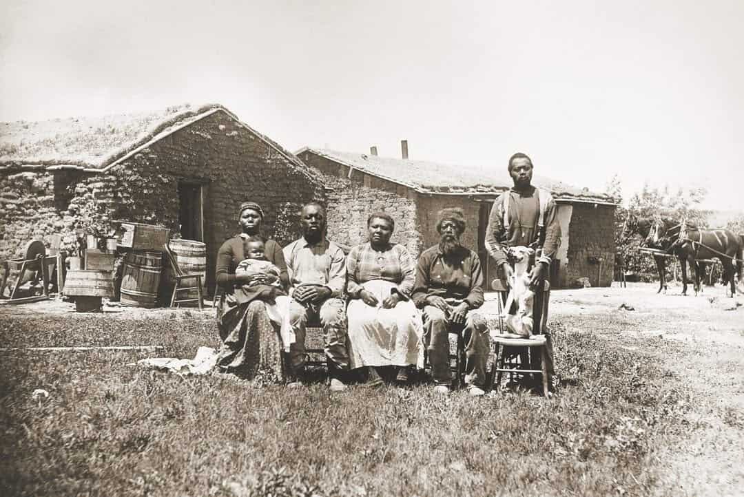 The Shores family seated in front of their sod house with chairs, barrels and a team of horses